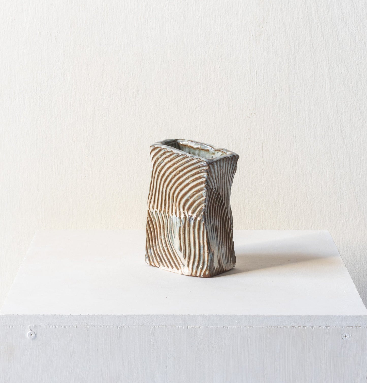 Ceramic vase with wavy texture on a white pedestal against a plain background