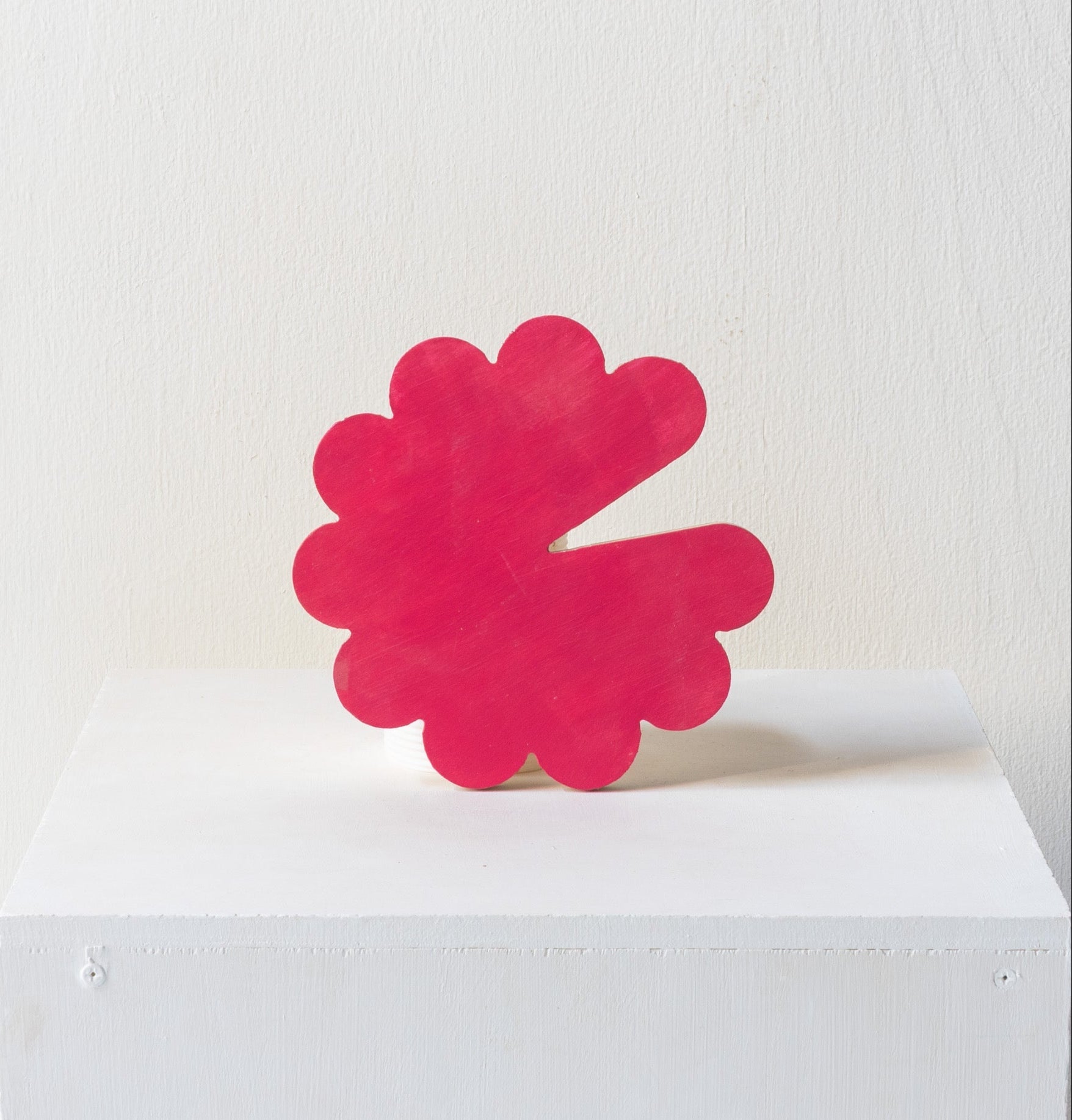 Pink abstract art piece on a white pedestal against a white background